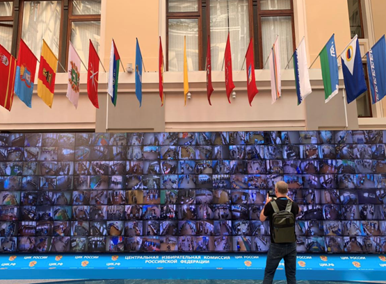 Bruno Kaufmann im Moskauer Fernsehstudio vor einer Wand mit Fernsehbildschirmen