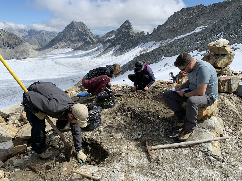 4 Personen arbeiten an einer archäologischen Ausgrabung in den Bergen